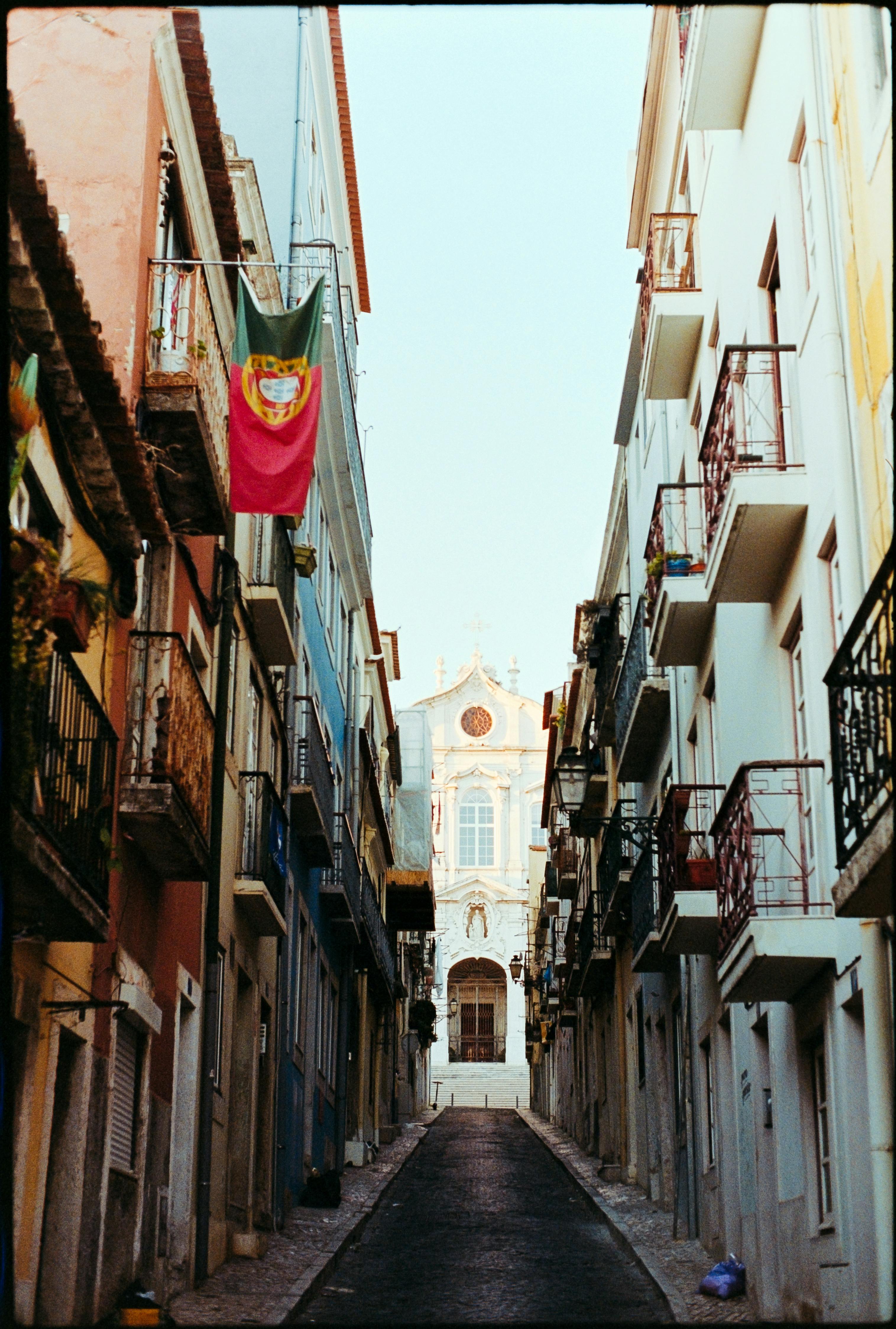 Discover the charm of a narrow street in Lisbon, Portugal, with colorful buildings and a Portuguese flag waving.