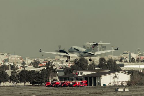 Free Airplane takes off over urban landscape with fire trucks ready at the fire station. Stock Photo