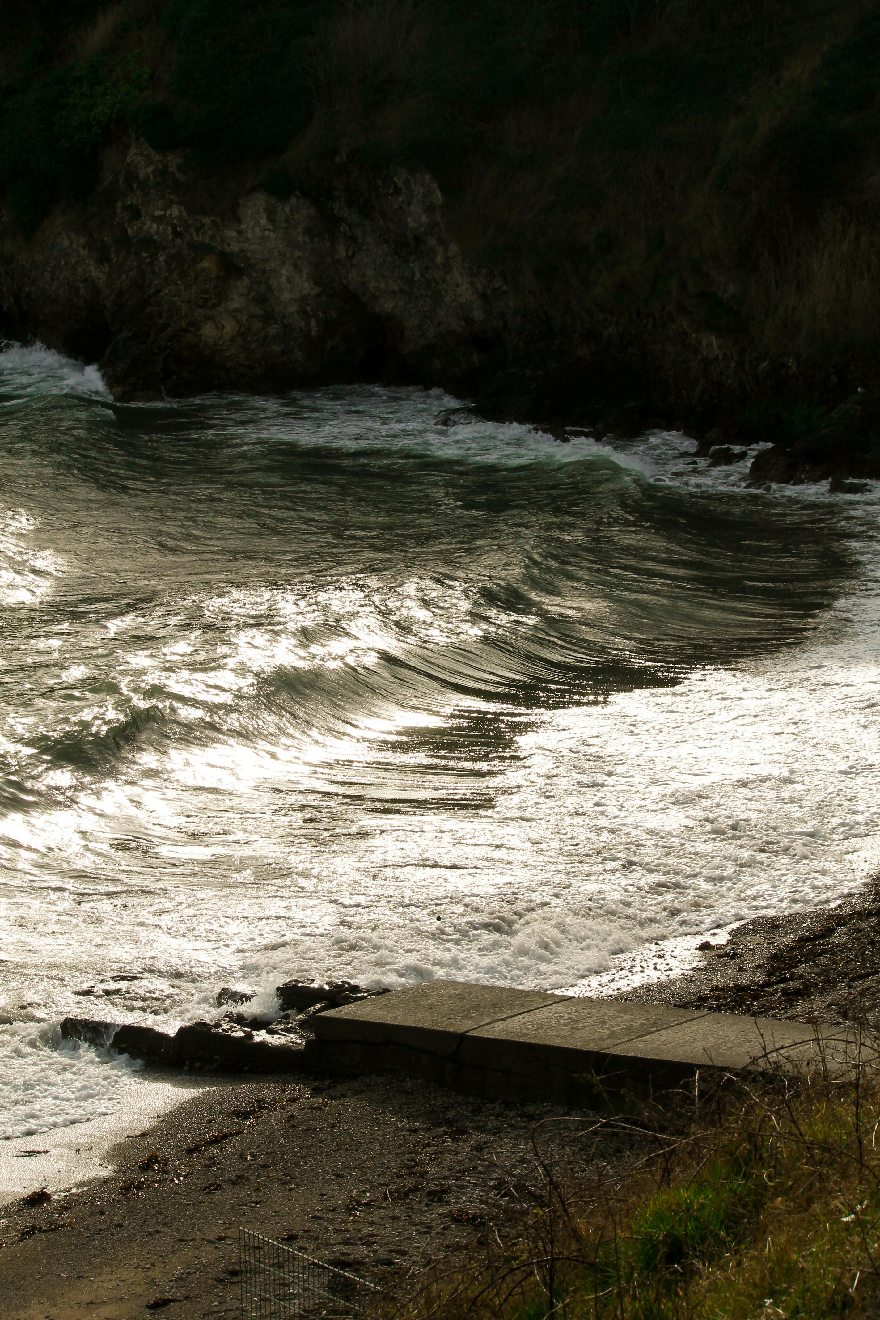 Dramatic coastline with waves crashing against a rocky beach under moody skies.