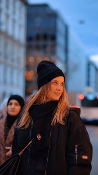 Portrait of a woman in a city setting during dusk, wearing a winter coat and beanie.