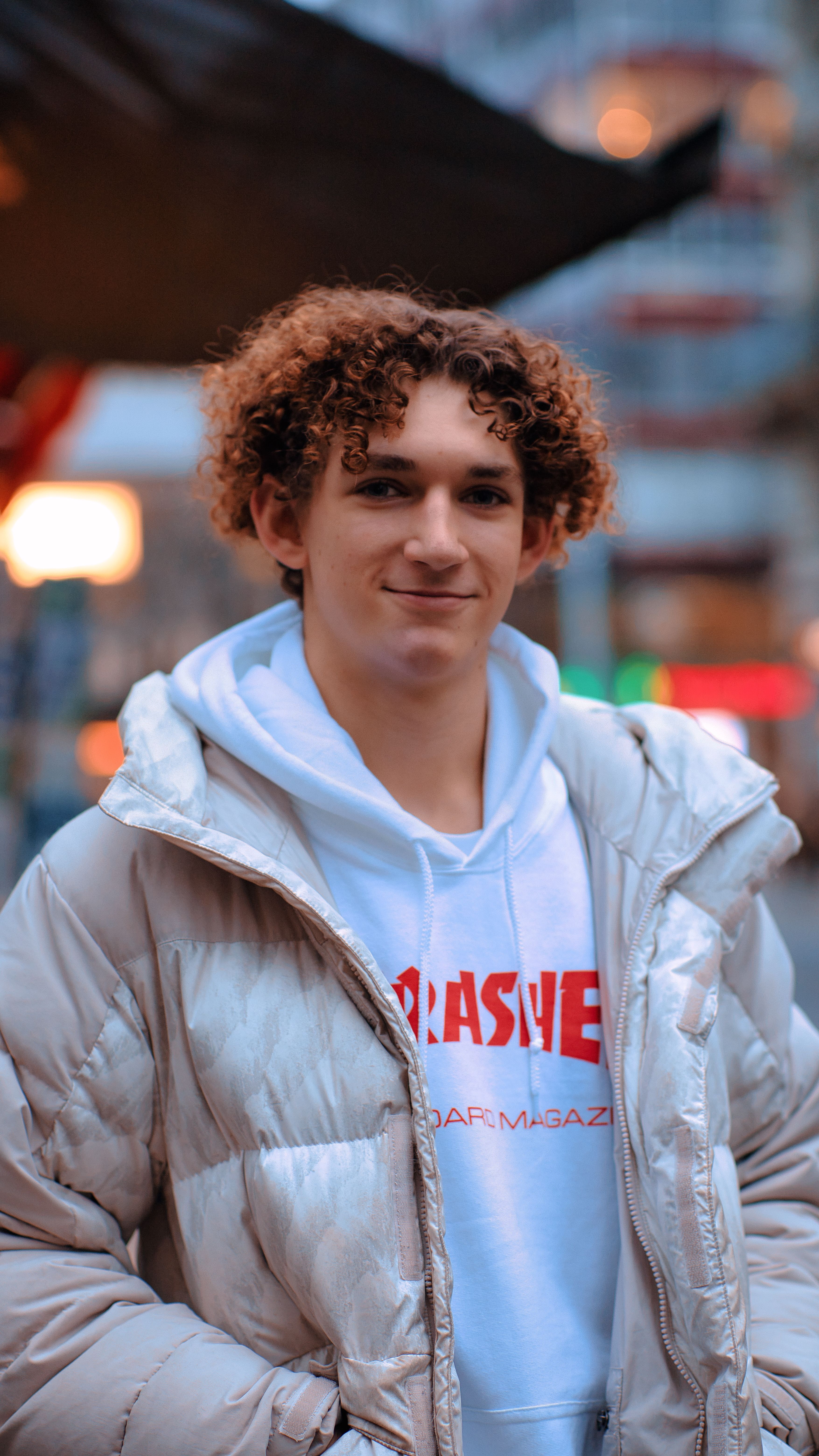 Stylish young man posing outdoors in a city, wearing a trendy winter coat and hoodie.