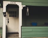 一座绿色房屋的门廊上，挂着一扇门，门上装饰着万圣节骨架