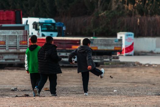 Three boys playing soccer in an urban setting of Ankara, Türkiye, during the day.