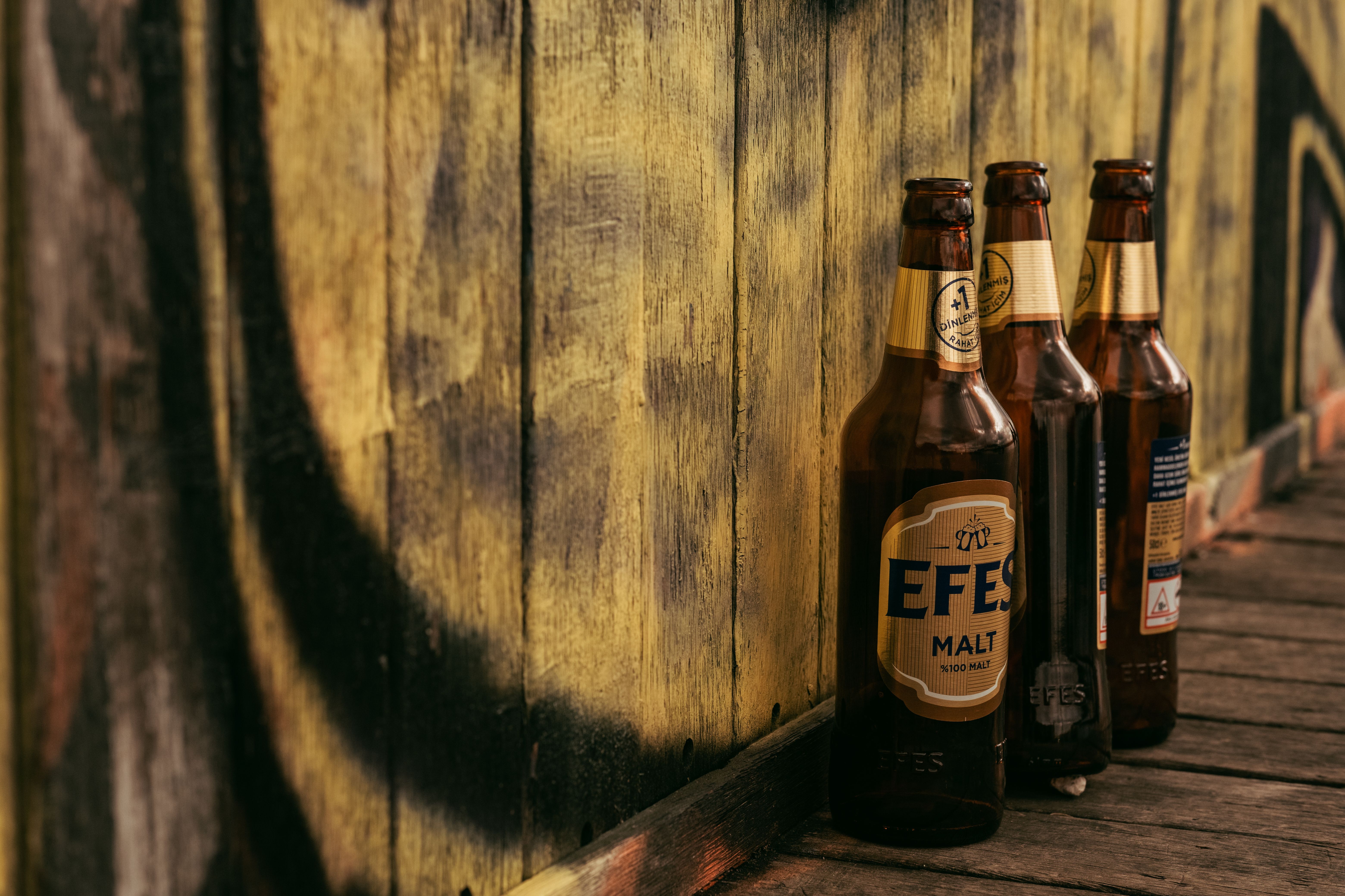 Three beer bottles on a wooden floor with a rustic painted background, creating a casual atmosphere.