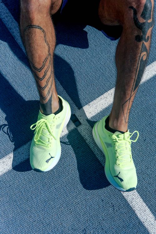 Free Runner with tattoos and neon shoes sitting on a sunlit track. Stock Photo