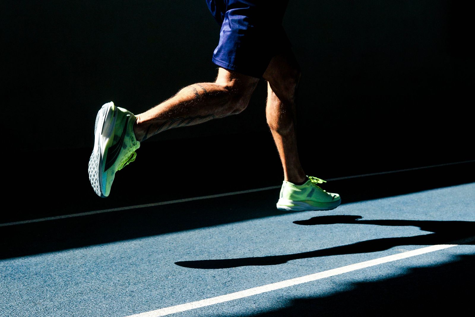 Runner's lower legs moving on a bright outdoor track