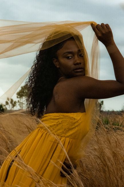 A woman in a yellow dress posing gracefully in a field of dry grass, exuding natural beauty.