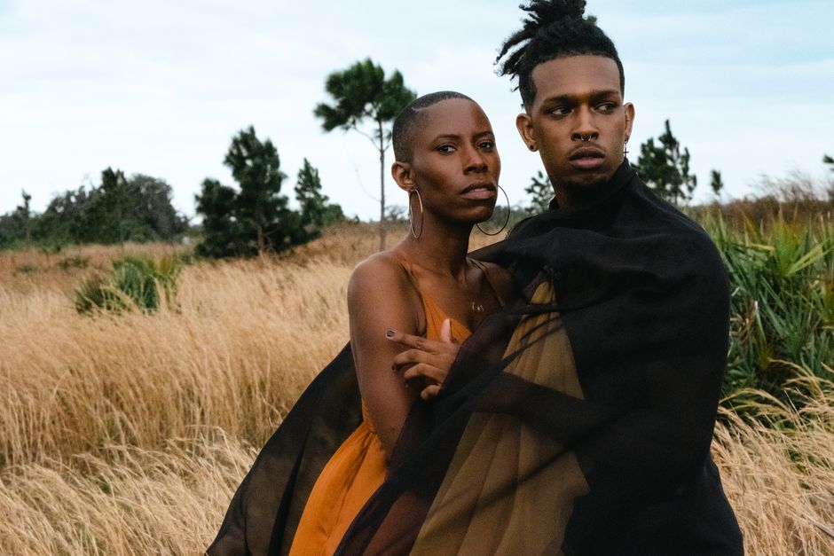 Stylish couple in elegant attire posing together in an open field, showcasing modern fashion.