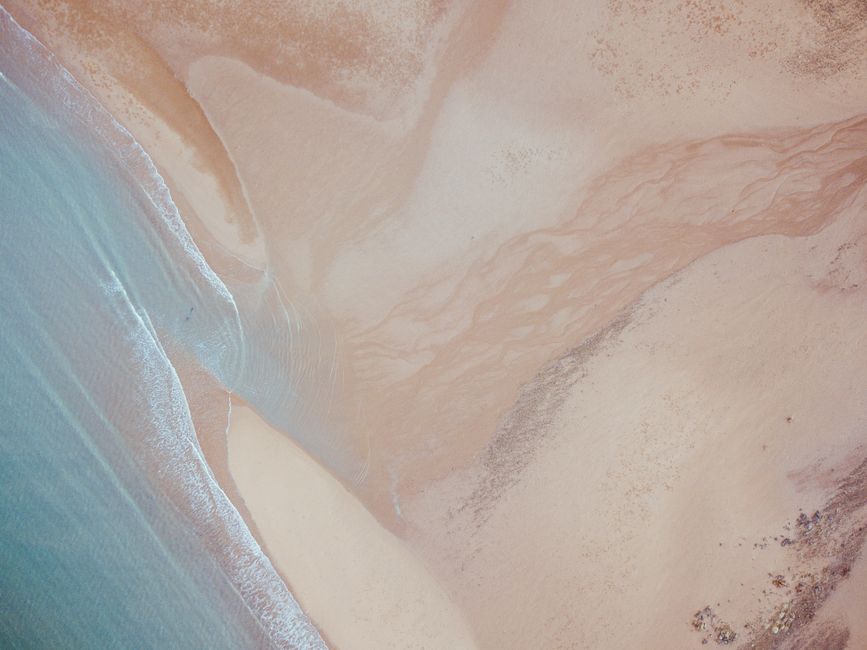 A top-down aerial shot of the sandy beach and ocean waves at Hay Point, Queensland, Australia.