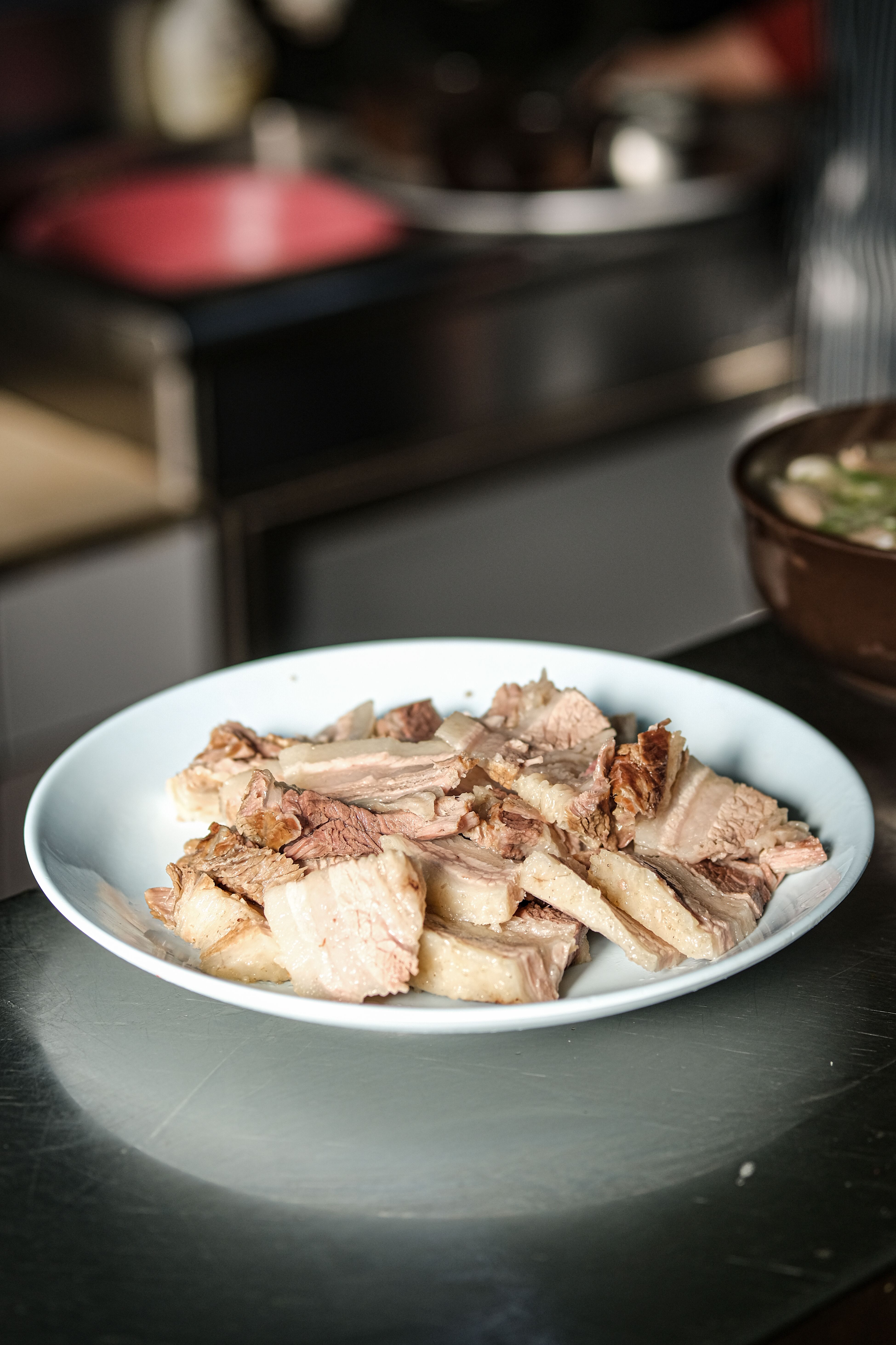 A bowl of shredded, sauce-glossed pulled pork next to an open Instant Pot with tongs resting on the rim.