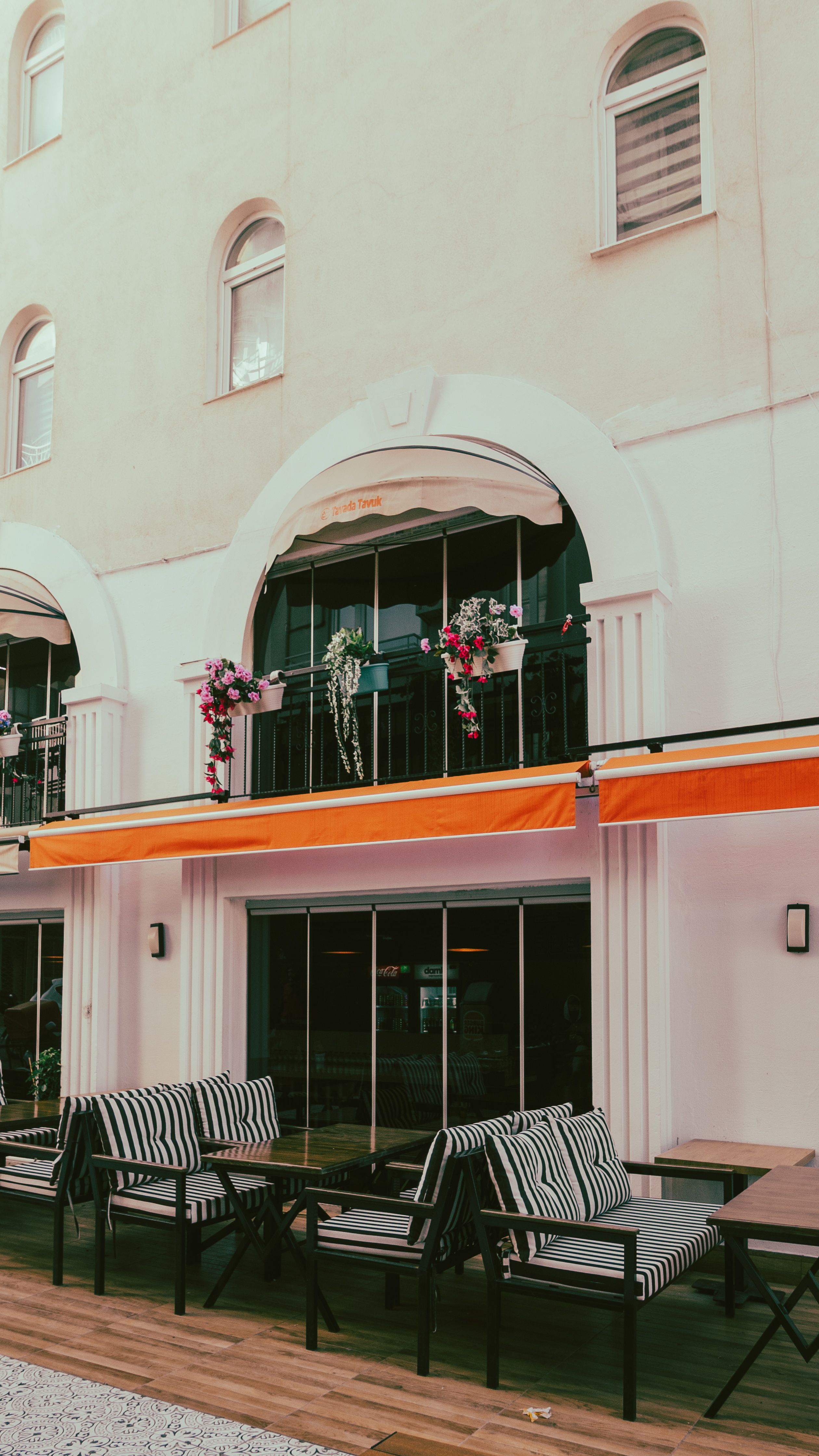 Empty urban terrace with striped armchairs and tables under vivid orange awnings.