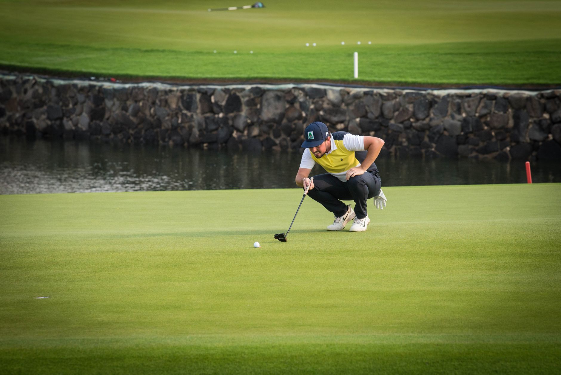 A golfer crouches to line up a putt on a sunny green.