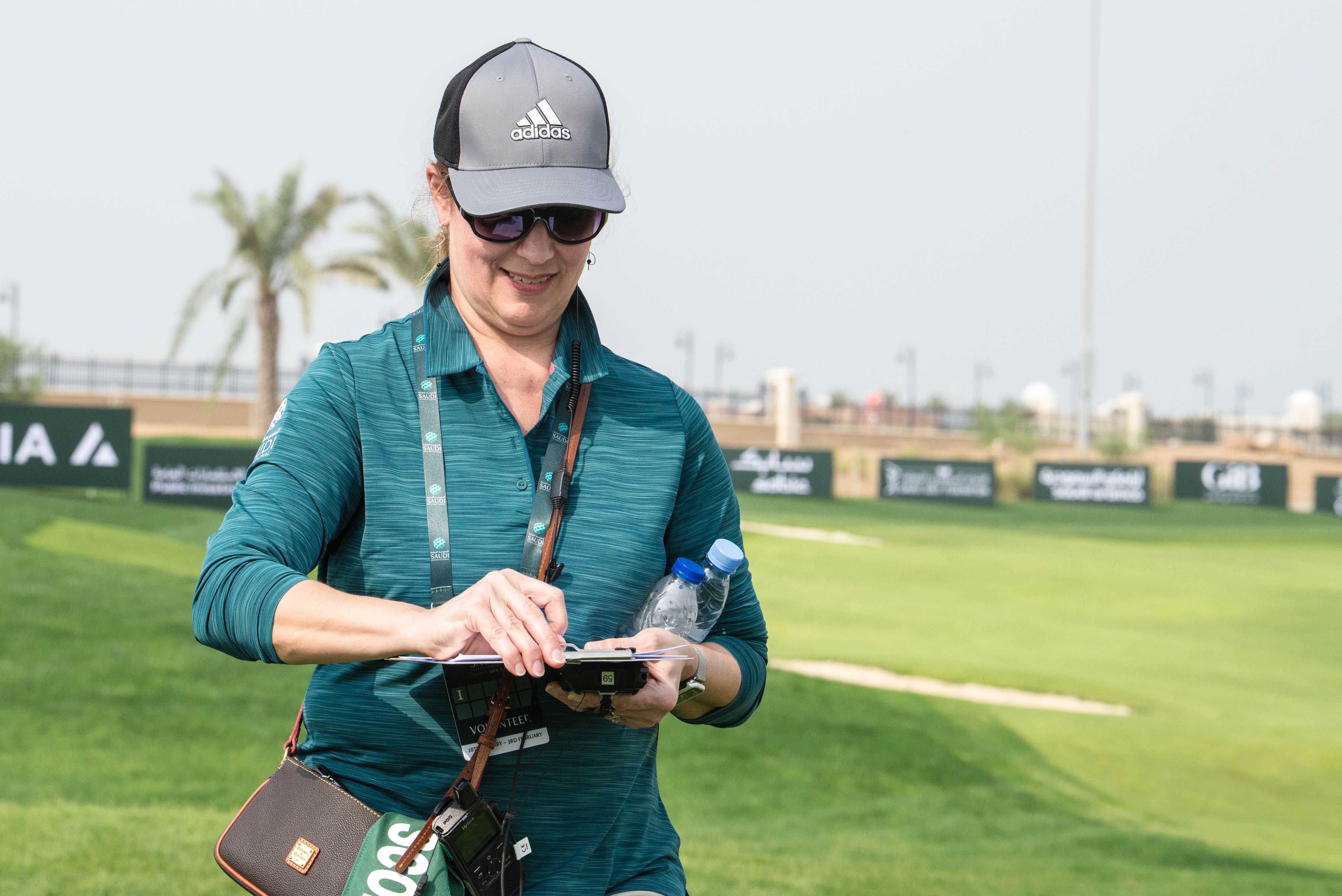 Smiling woman in sunglasses and cap on a golf course, enjoying sunny day.