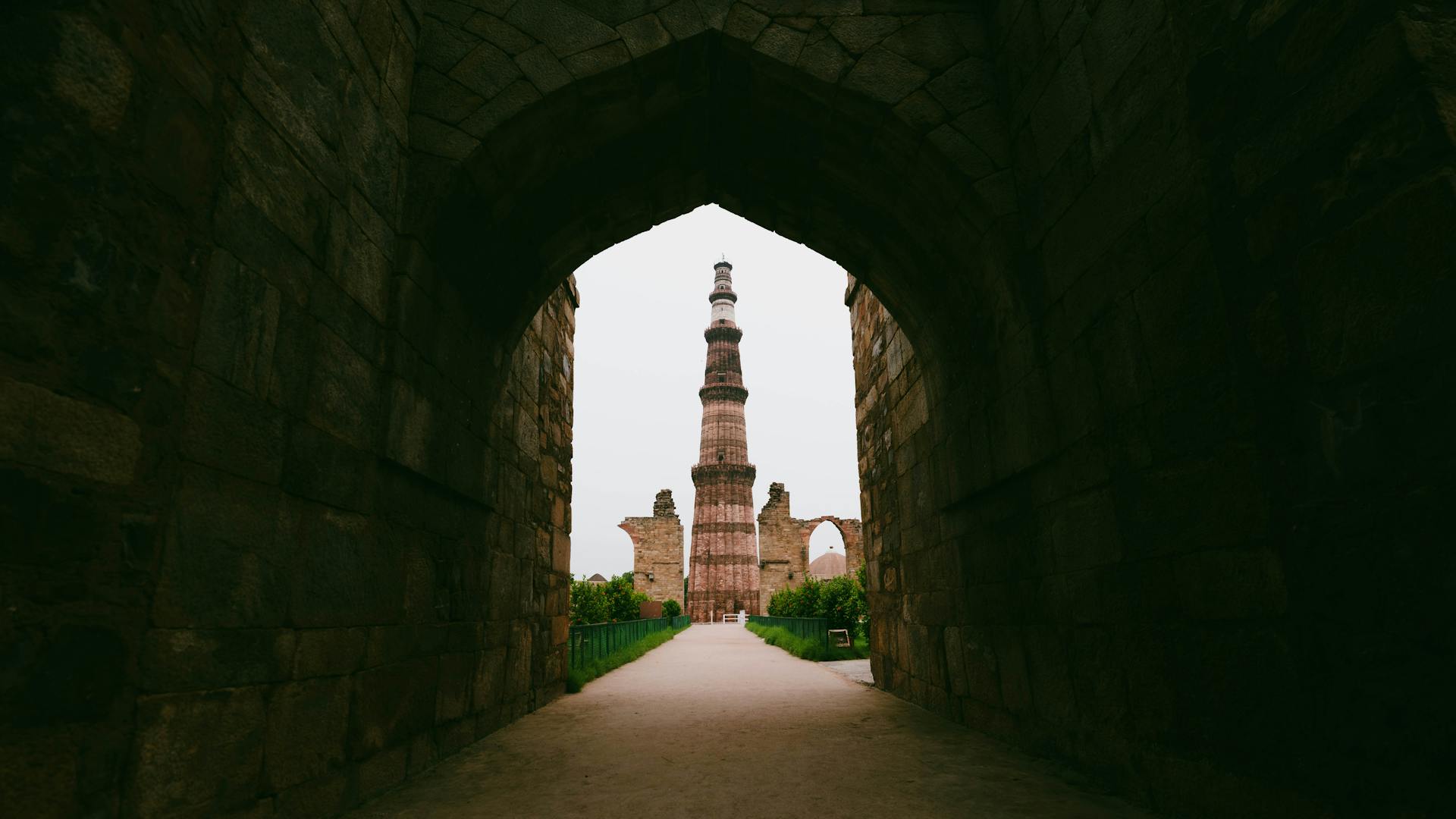 Qutub Minar viewed through a historic stone archway, showcasing architectural grandeur.