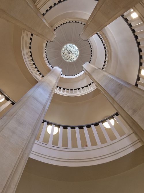Free Elegant view of a circular stairwell featuring tall ornamented columns and intricate ceiling design. Stock Photo