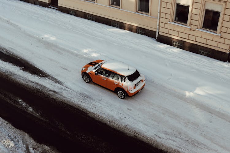 Aerial View Of A Car Driving On Snowy Street Near A Residential Building In City 