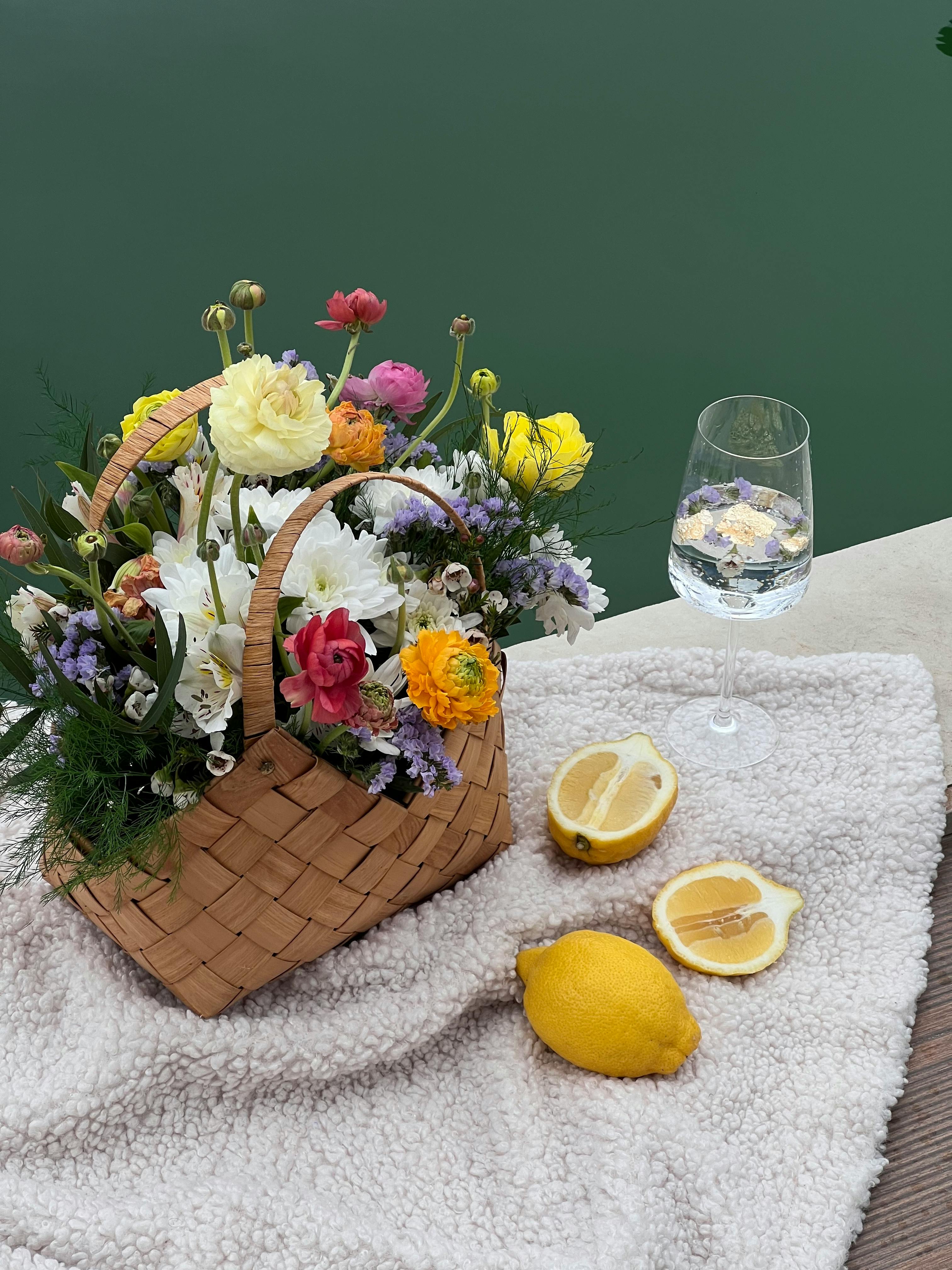 bunch of flowers in a basket next to a glass and lemon