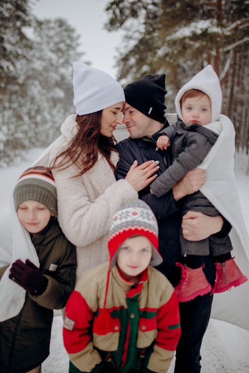 Free A joyful family of five enjoying a snowy winter day together wrapped in blankets outdoors. Stock Photo
