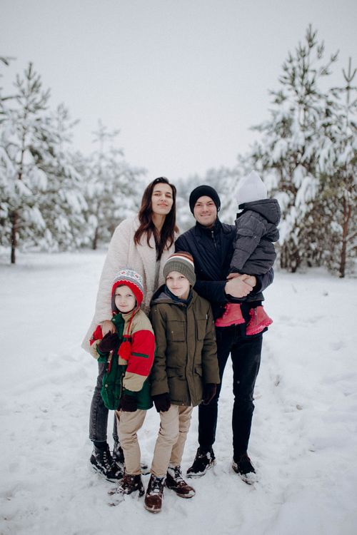 Free A joyful family dressed warmly, posing together in a snowy forest during winter. Stock Photo