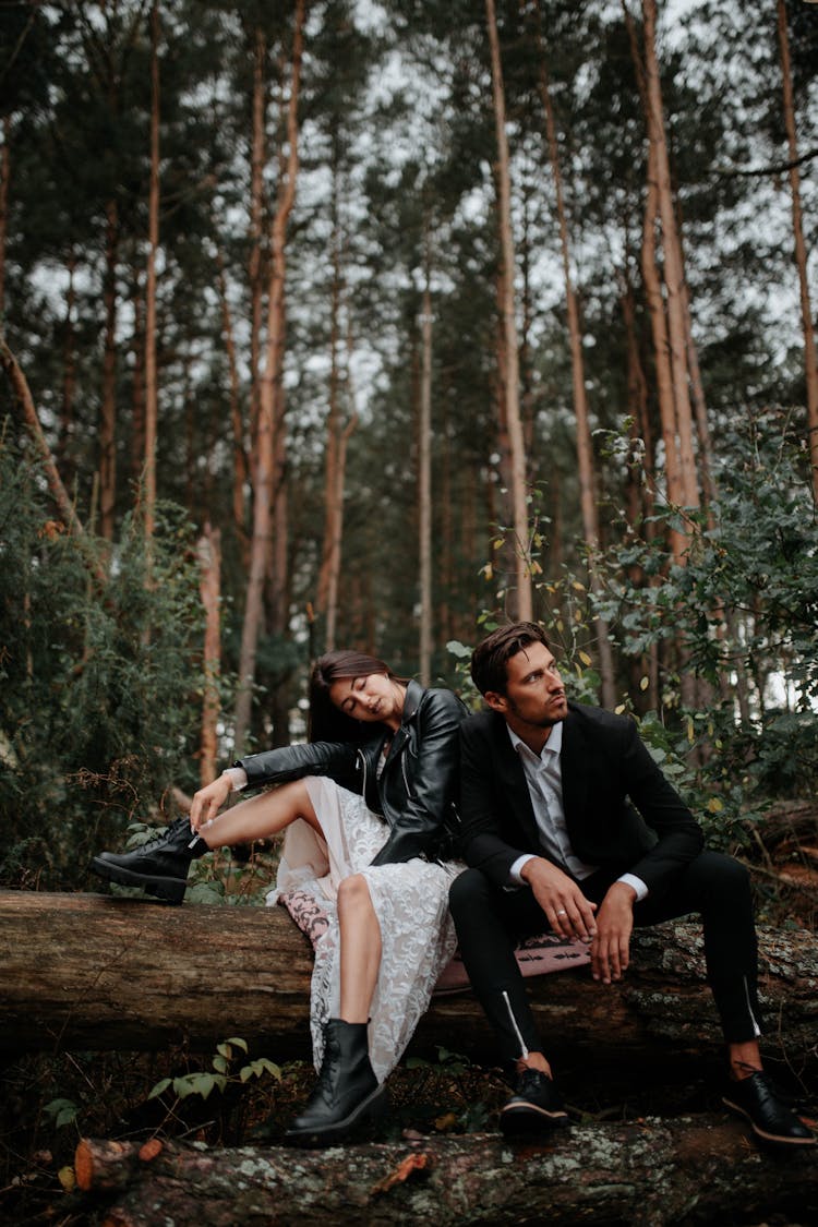 Fashionable Man And Woman Sitting On A Log In The Forest 