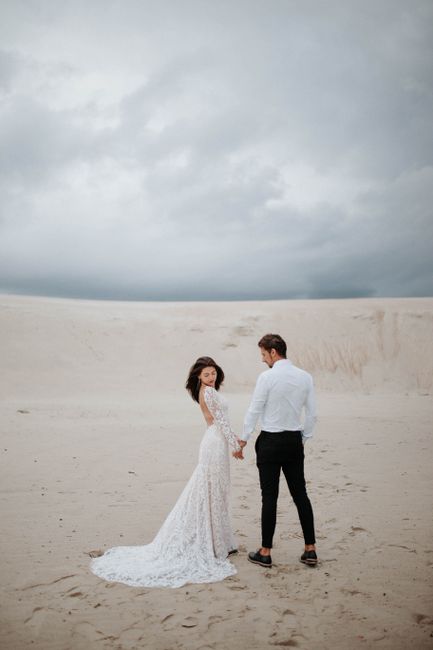 Newlywed couple in wedding attire holding hands on a serene beach.