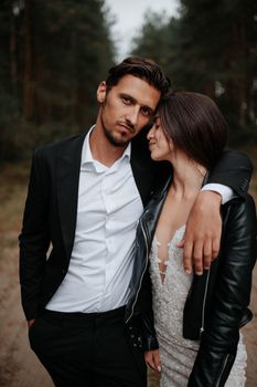 Couple in elegant wedding attire embracing in a scenic forest setting.