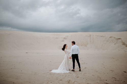 Free Bride and groom holding hands in a desert landscape, showcasing love. Stock Photo