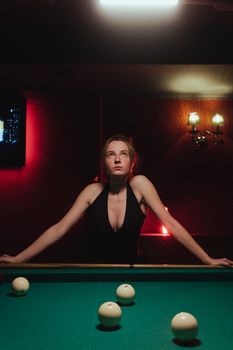 A woman in a black dress playing billiards in a dimly lit club setting with elegant lighting.