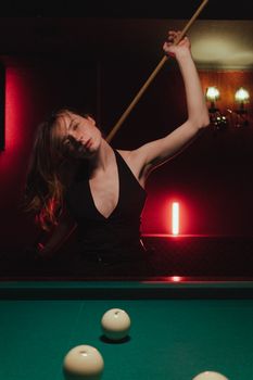 A woman plays billiards, holding a cue stick in a dimly lit nightclub, evoking a nightlife atmosphere.