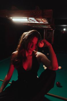 A woman with long brown hair poses moodily at a billiard table under dim nightclub lights.