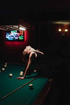 Woman posing dramatically on a pool table in dim lighting for a glamorous ambiance.