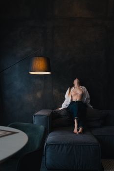 Artistic portrait of a woman sitting on a dark sofa under soft lamp light, creating a moody atmosphere.