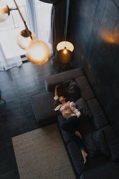 Stylish woman posing on dark modern sofa, captured from above, in a chic indoor setting.