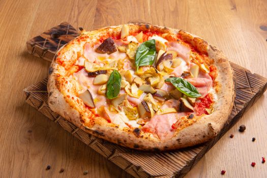 Capricciosa pizza with cheese, bacon, tomatoes, mushrooms and basil, italian meal. Baked neapolitan pizza with artichokes served on wooden board.
