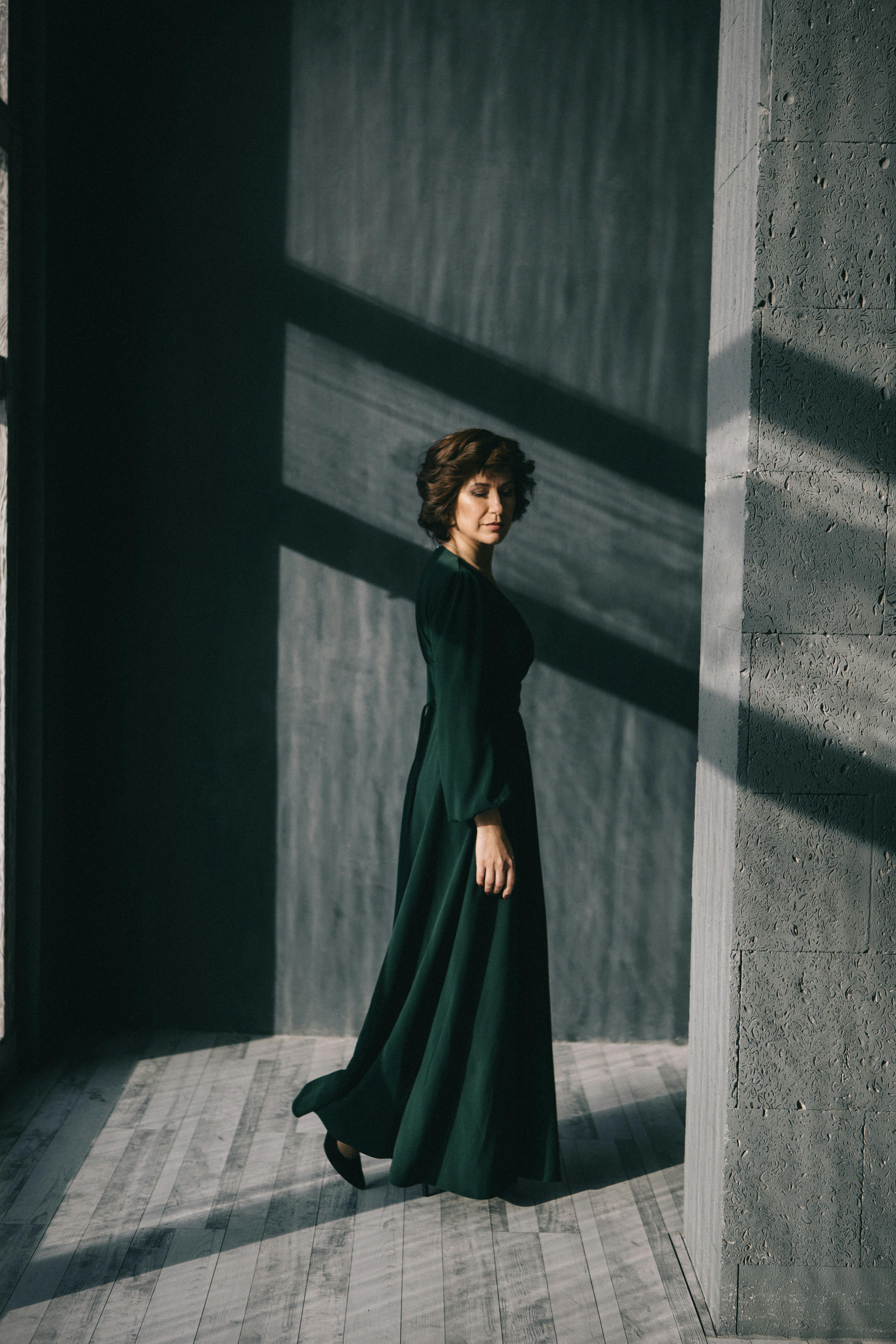 Enigmatic woman in a long dress, captured with dramatic lighting indoors.