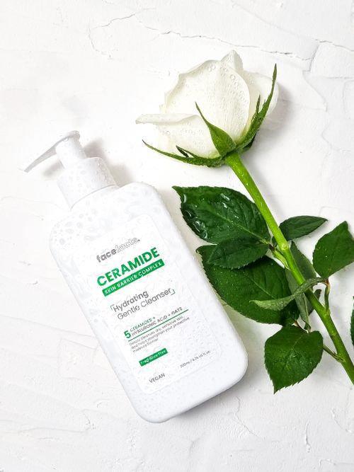Free Ceramide hydrating gentle cleanser bottle with a white rose on a textured background. Stock Photo