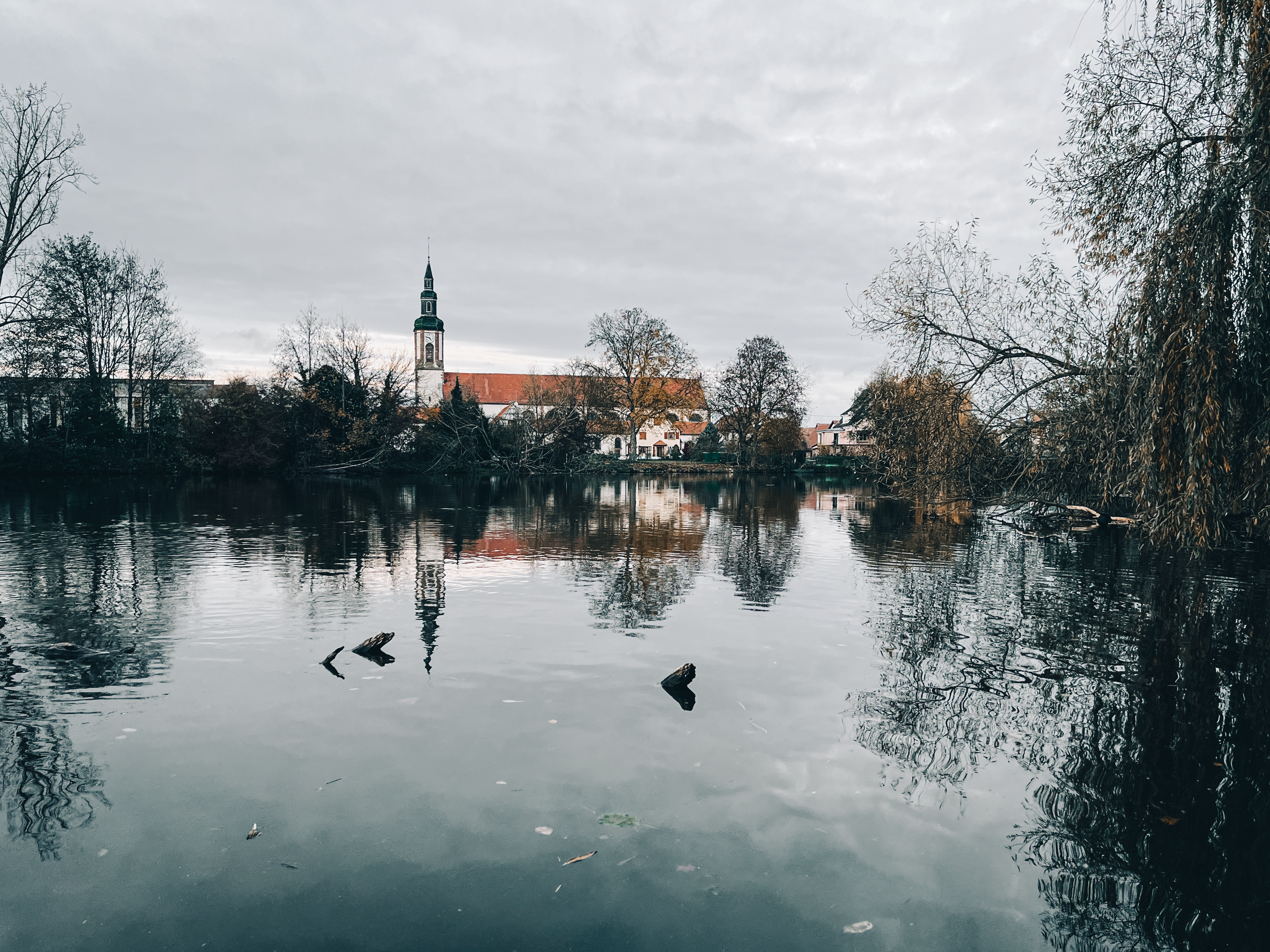 Tranquil autumn scene of a church and town reflecting on a calm river with bare trees.