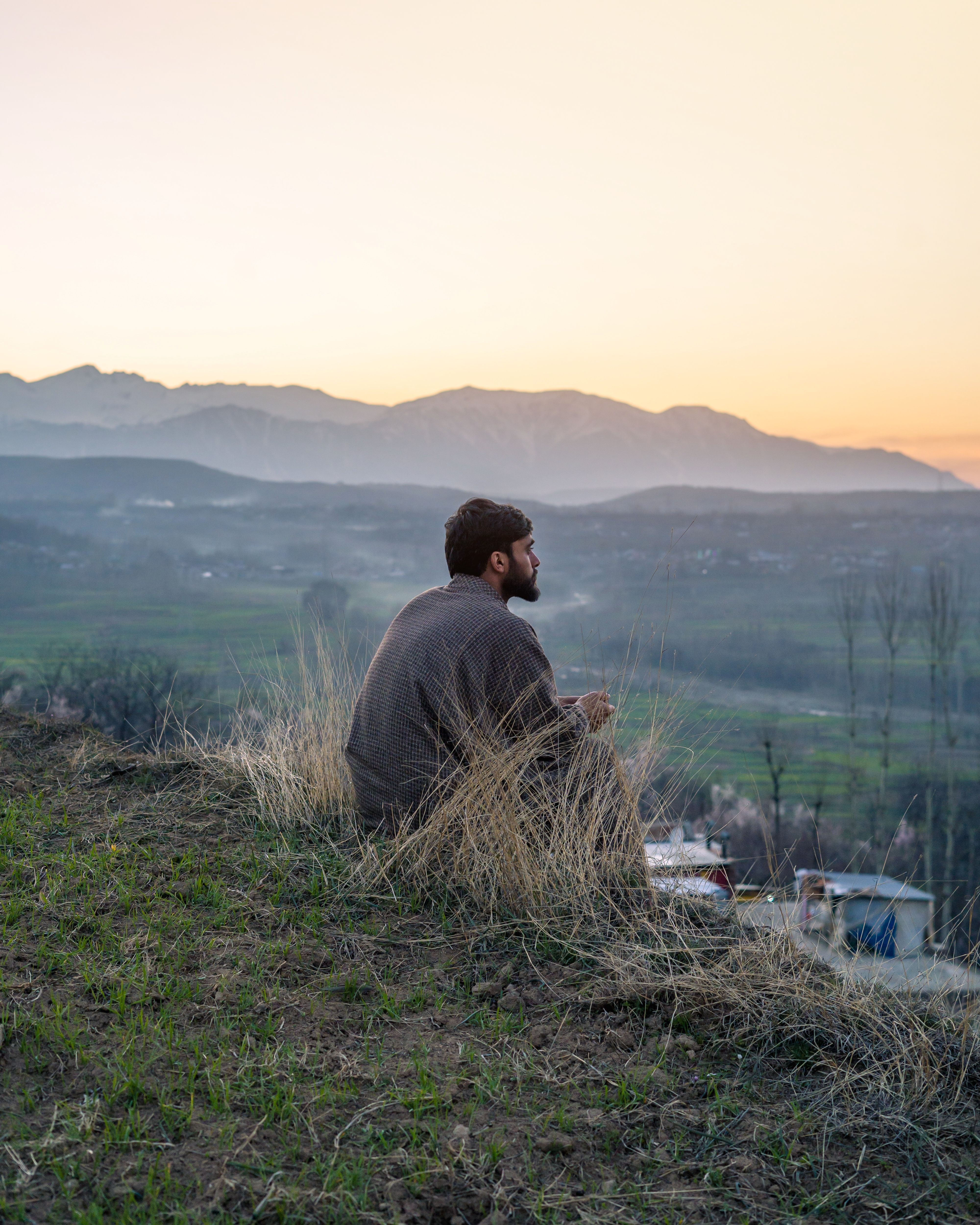 A Man Sitting on Top of a Hill and Looking at the Sunset with Mountains ...