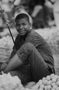 Black and white portrait of a smiling merchant in a bustling market with produce.