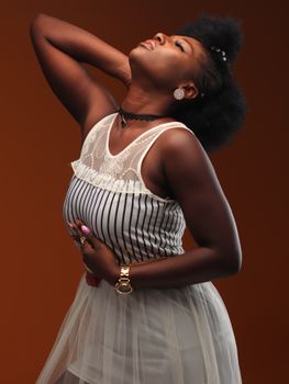 Portrait of an elegant woman posing in a studio setting, showcasing her afro hairstyle and stylish outfit.