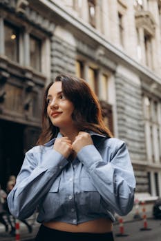Young woman in a blue shirt smiling confidently in an urban city setting.