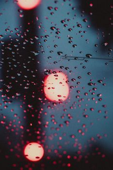 Artistic view of raindrops on glass with defocused red city lights at night.