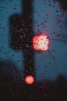 Raindrops on window with blurred red traffic light creating a moody evening atmosphere.