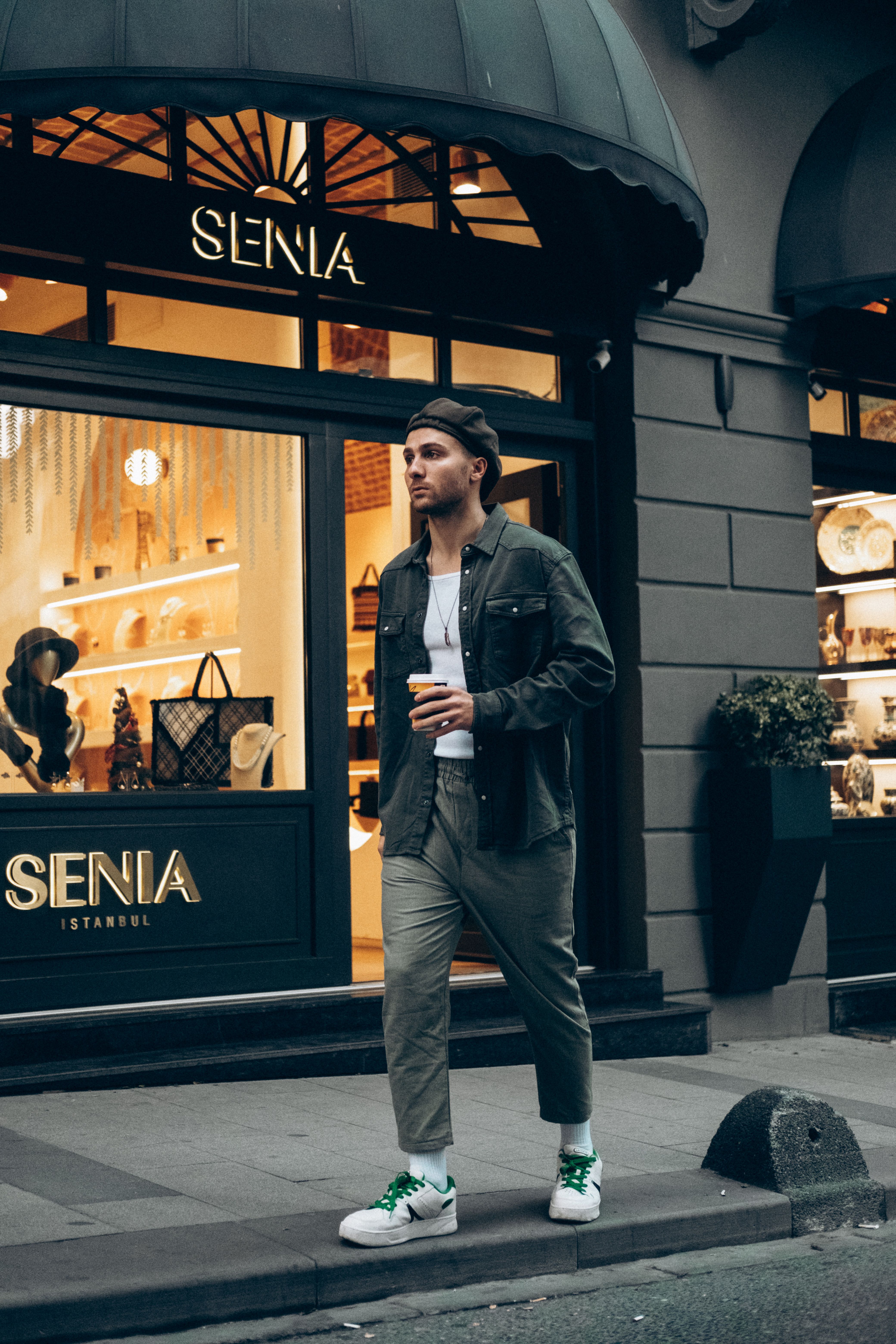 Casual fashion portrait of a man in an urban setting, holding coffee and walking past a boutique.
