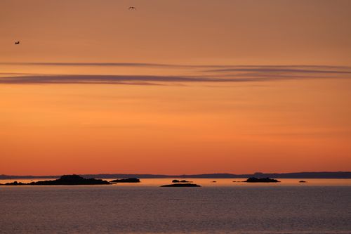 Free Tranquil view of an orange sunset over a calm ocean with distant islands. Stock Photo