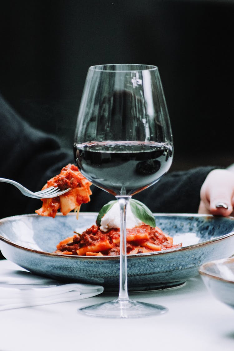 Woman Eating Pasta And Drinking Wine In Restaurant