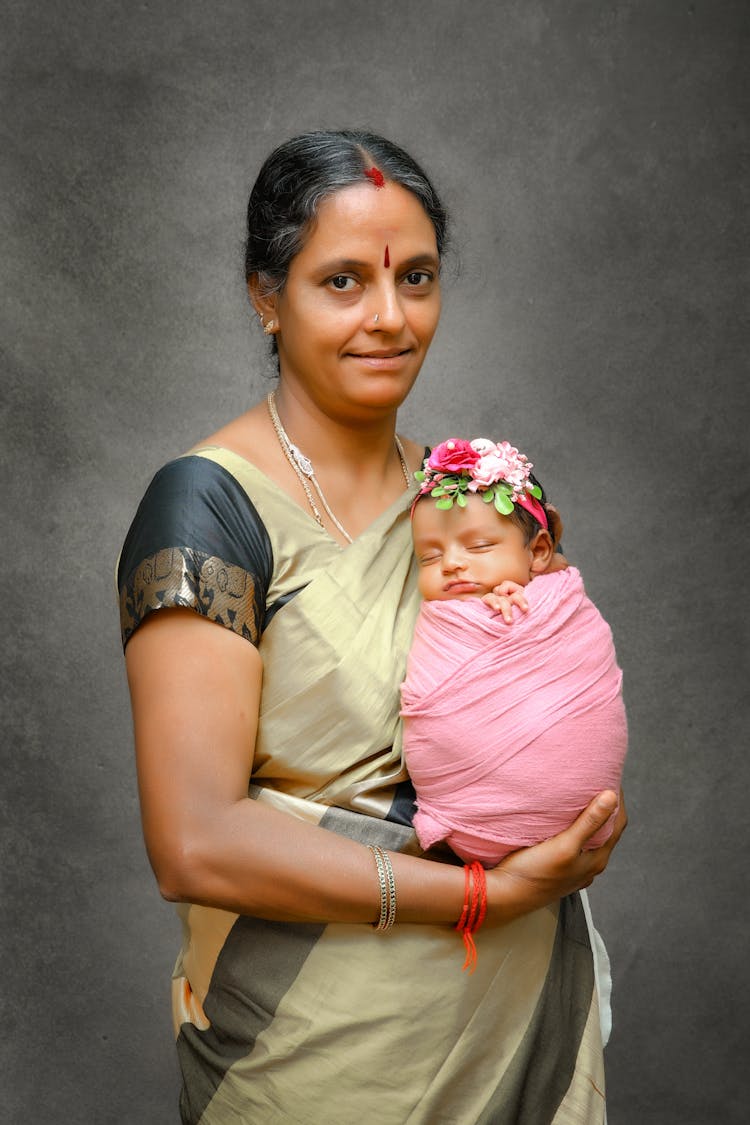 A Woman In Traditional Indian Clothing Holding A Newborn