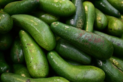 Close-up of green avocados piled up at a market offering fresh produce.
