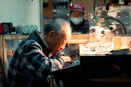 Free An elderly watchmaker meticulously repairs a watch in a dimly lit workshop, symbolizing dedication to craft. Stock Photo