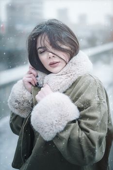 Elegant portrait of a woman in a fur-lined jacket amidst falling snowflakes in Ardabil, Iran.